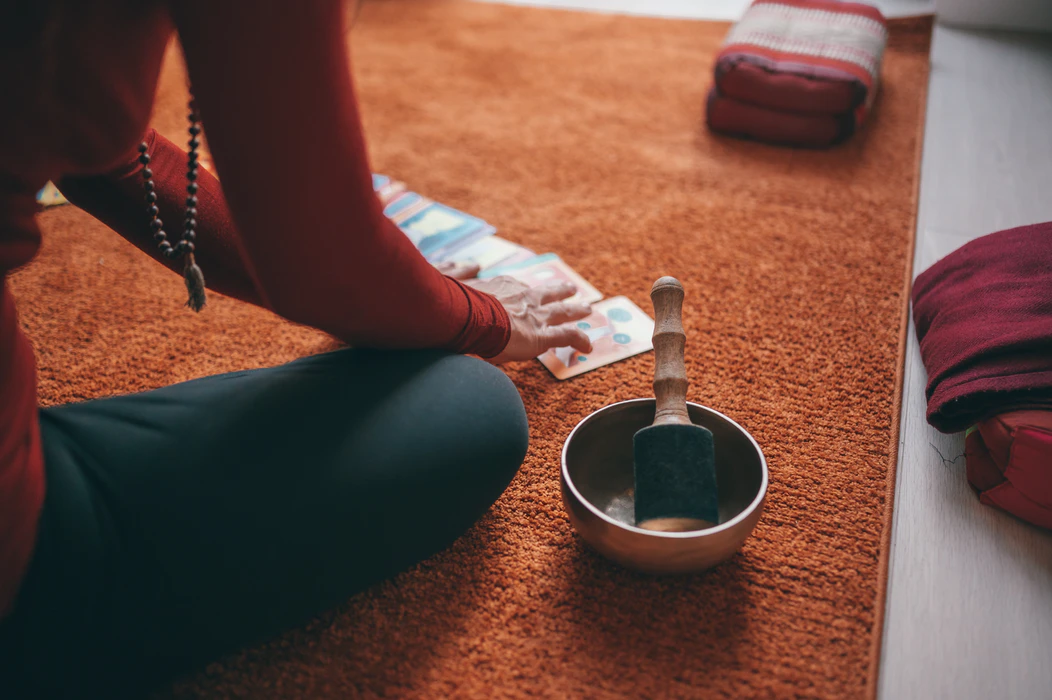 A woman playing with cards on the floor with a meditation bowl (Conscious Design/UnSplash).