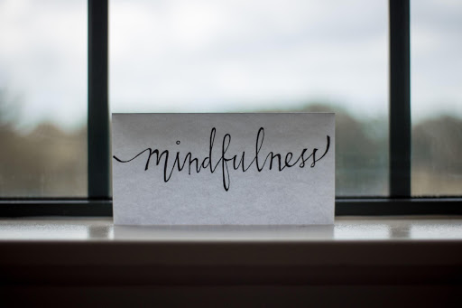 a sheet of paper with the word mindfulness written in black ink perched on a window sill