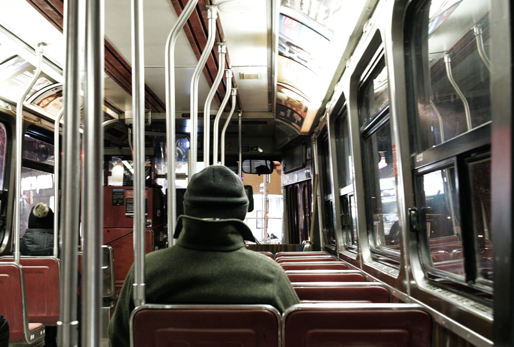 a view from inside a train with a person sitting facing away from the camera sitting on red seats