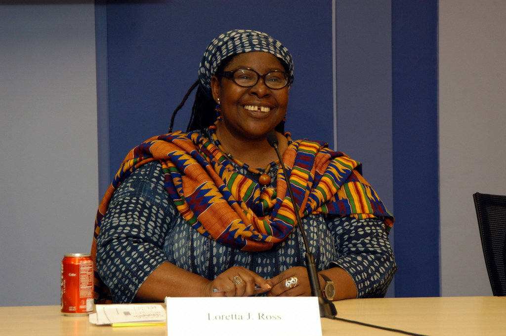 a woman with glasses sits at a brown desk smiling straight ahead