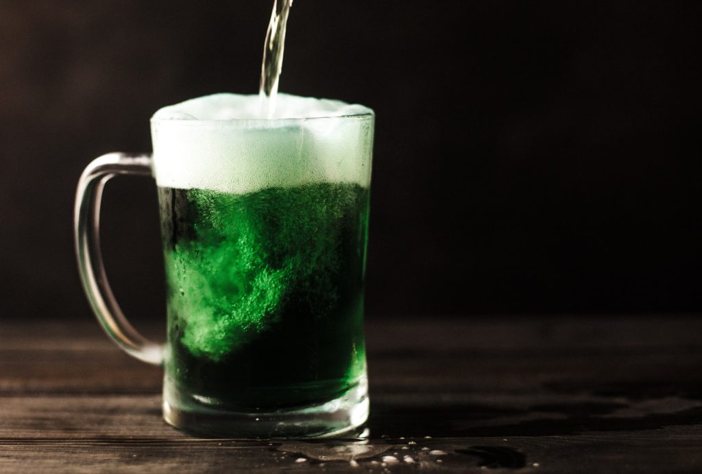 liquid is poured into a green alcoholic drink in a mug on a dark wooden table