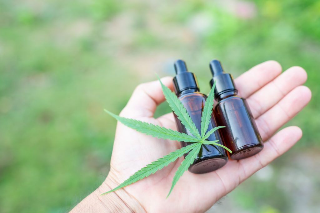 a white hand holds two cannabis bottles and a mairjuana leaf