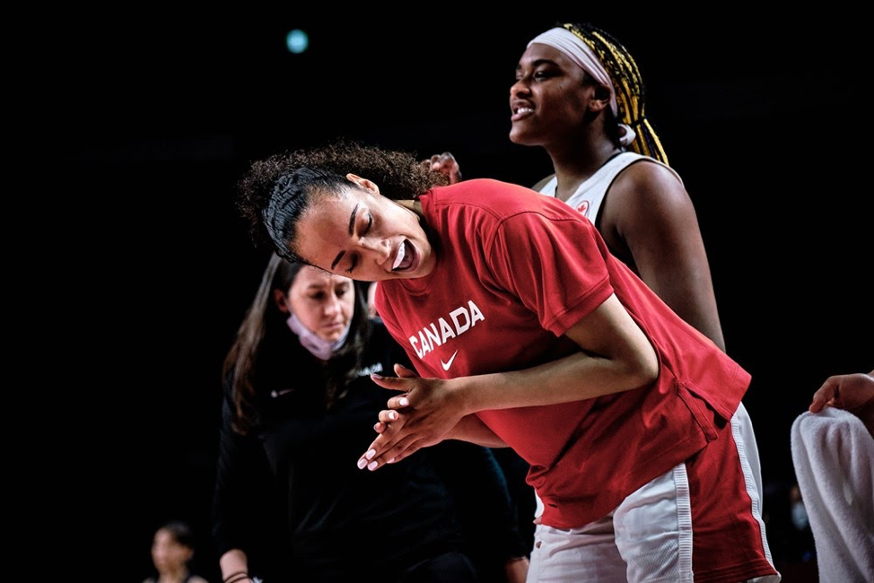 Two women basketball players in foreground, coach Carly Clarke in background