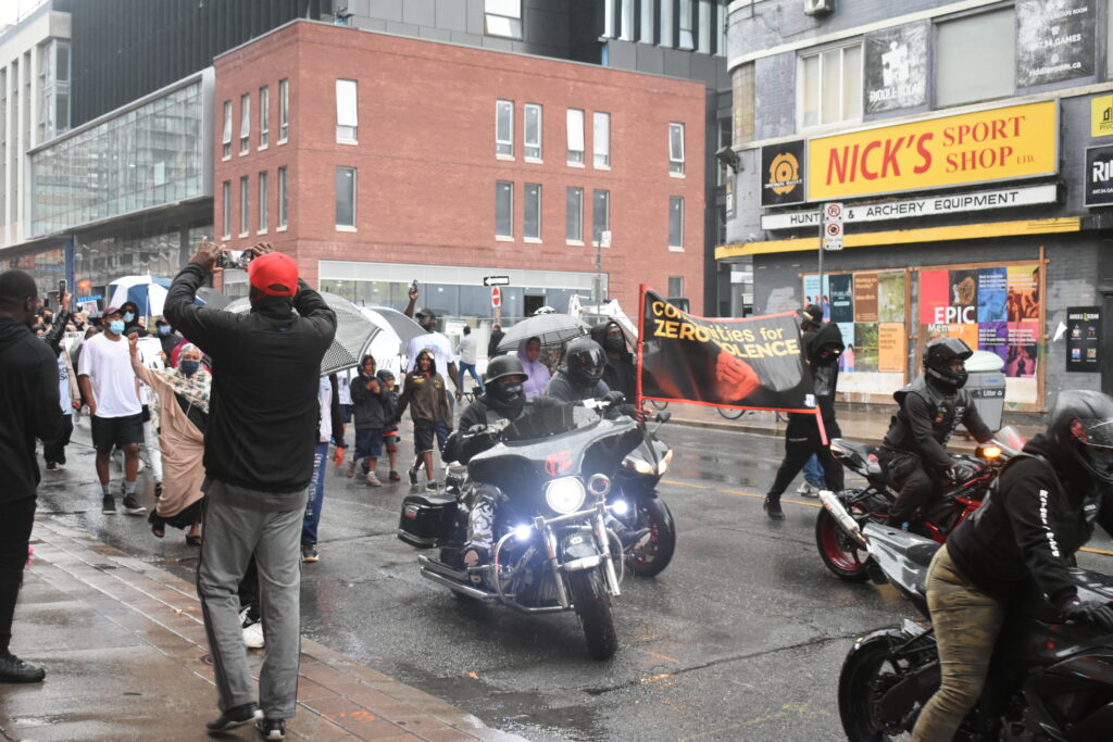 Bikers and people walking down a street. They hold signs protesting gun violence.