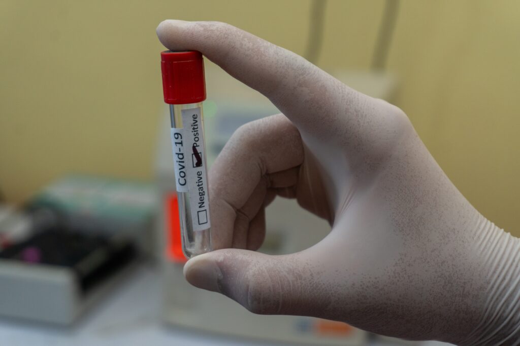 A photo of a gloved hand holding a test tube labelled COVID-19.