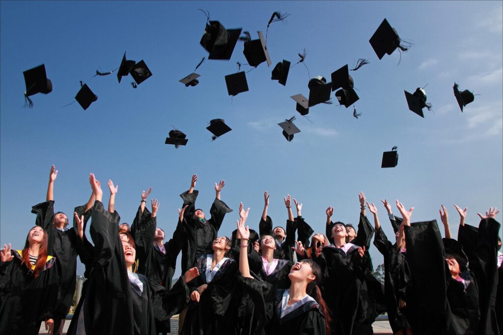 Students celebrate graduation and throw their black graduation caps in the air on sunny day.