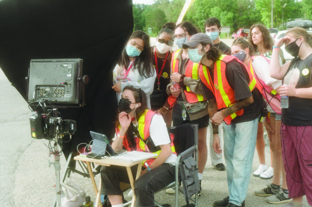 Multiple people in constructions vests and masks behind the scenes of film set.