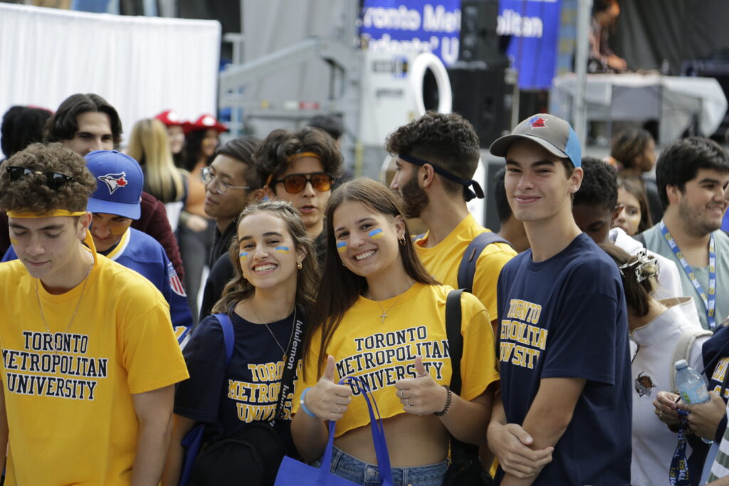 Four students in yellow and navy Toronto Metropolitan University merch smile for the picture