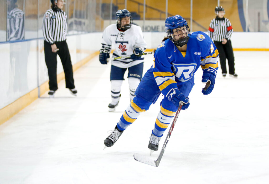Women's hockey player wearing blue jersey skates up the ice