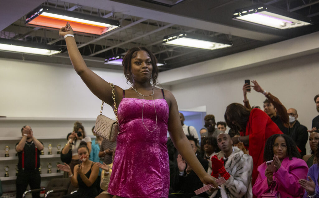 A woman in a hot pink dress poses at the end of a runway.