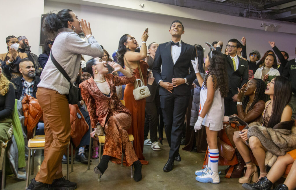 A man in a tuxedo walks through a cheering crowd.