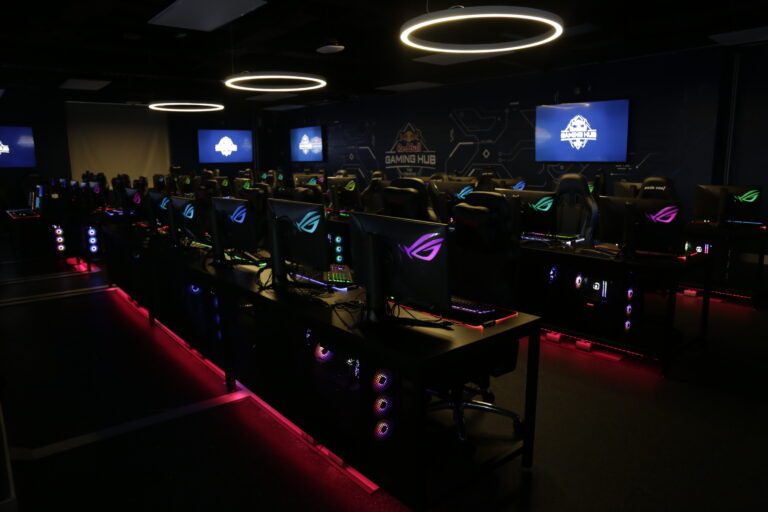 A dark room filled with state-of-the-art computers and gamer chairs.
