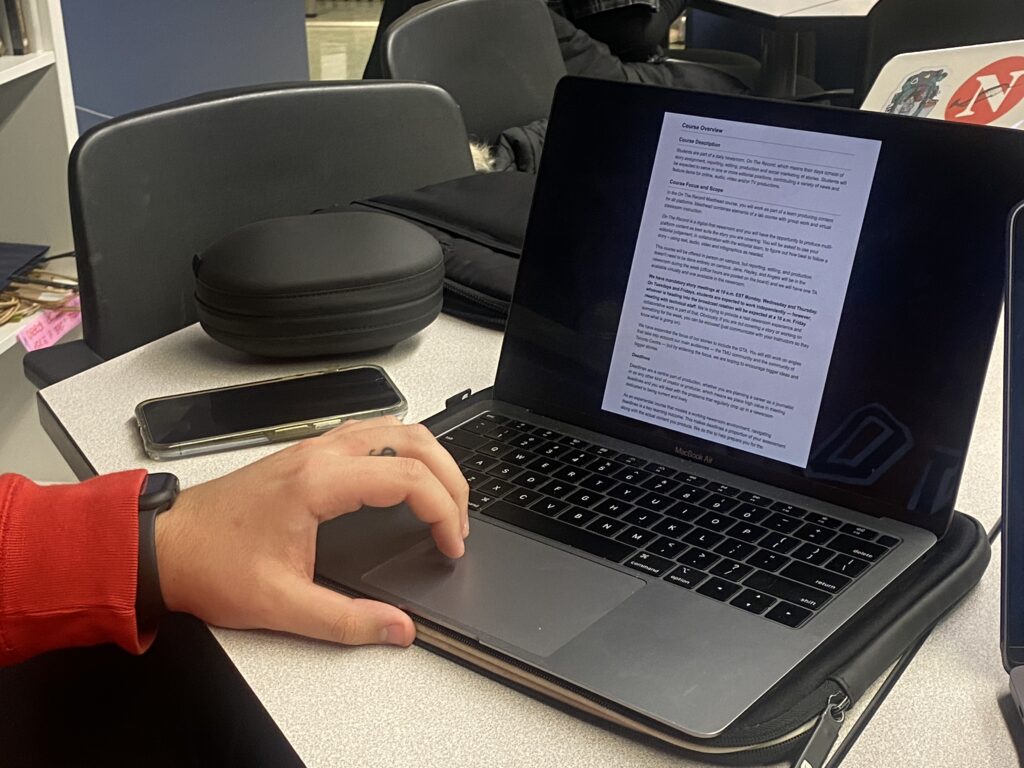 A man's hand scrolls through a document on a laptop.