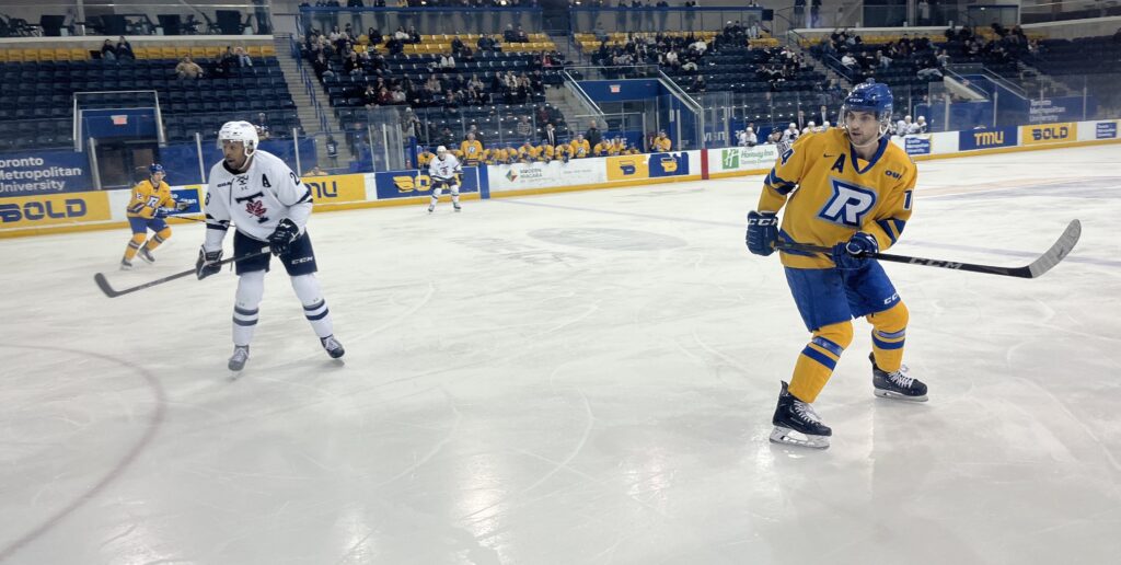 A hockey player waits for a pass, as an opposing player looks on nearby.