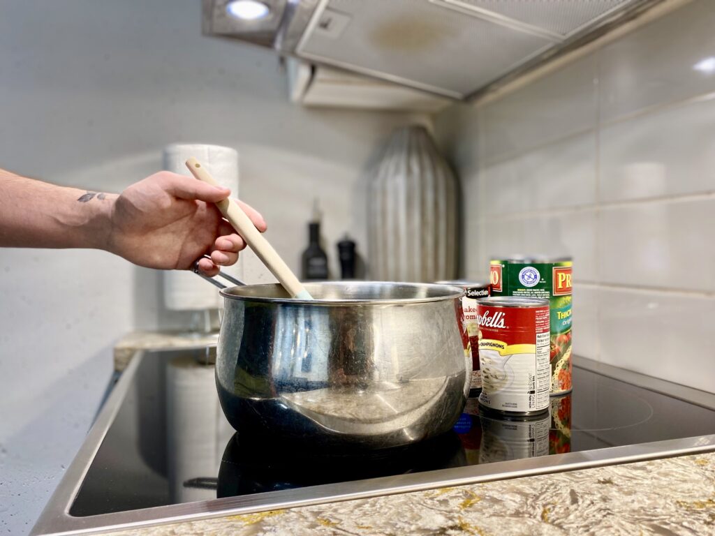 A pot on a stove with cans in the background.