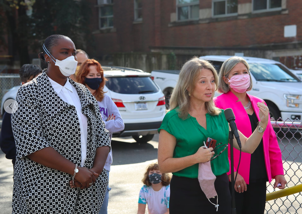 Marit Stiles giving a speech in a green top in front of a parking lot