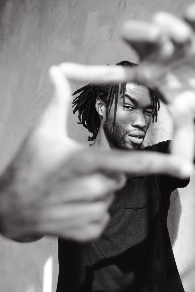 Black and white photo of a Black man holding his hands in a portrait frame shape.