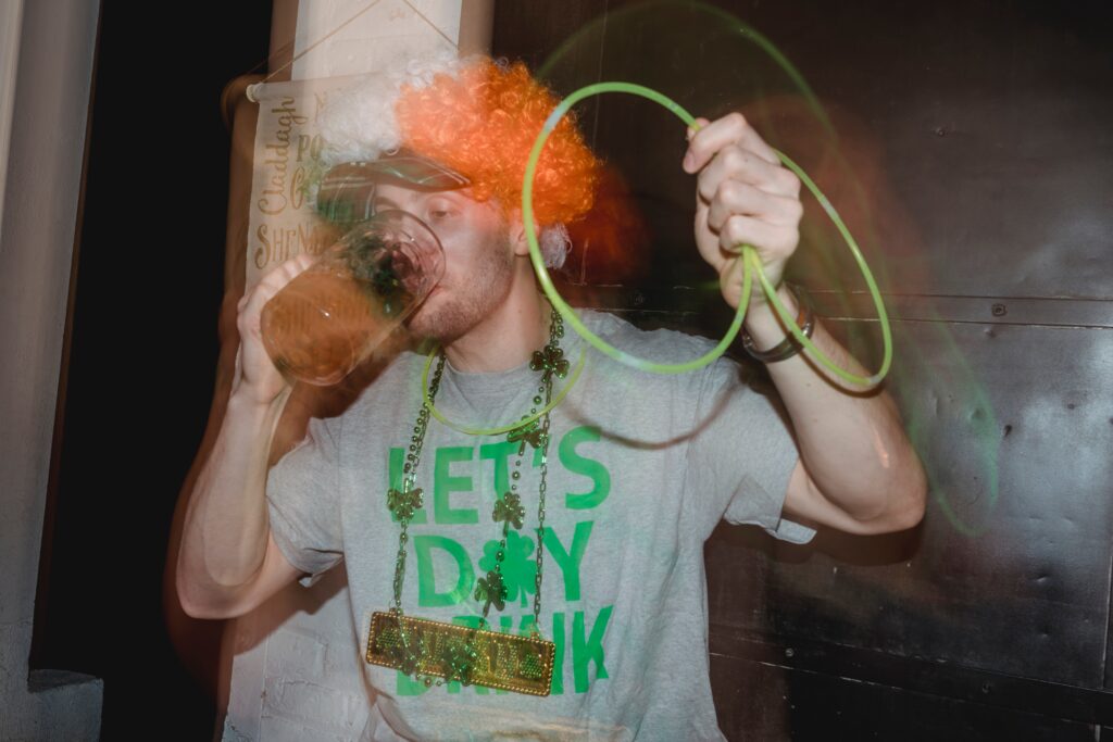 A hazy man in St. Patrick's Day paraphernalia chugs a pint of beer.