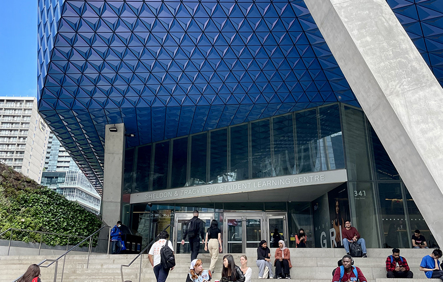 Photo of the outside of the SLC at TMU (a blue windowed building) with students out front.