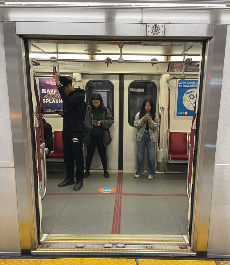 Three commuters stand on the Line 1 subway looking at their phones, as the doors open.