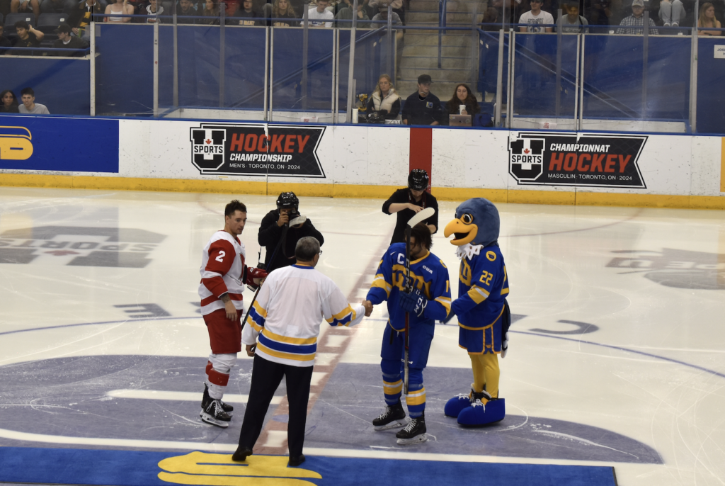 TMU falcon mascot Franke B. Bold in a falcon costume on the ice at Mattamy with hockey players.
