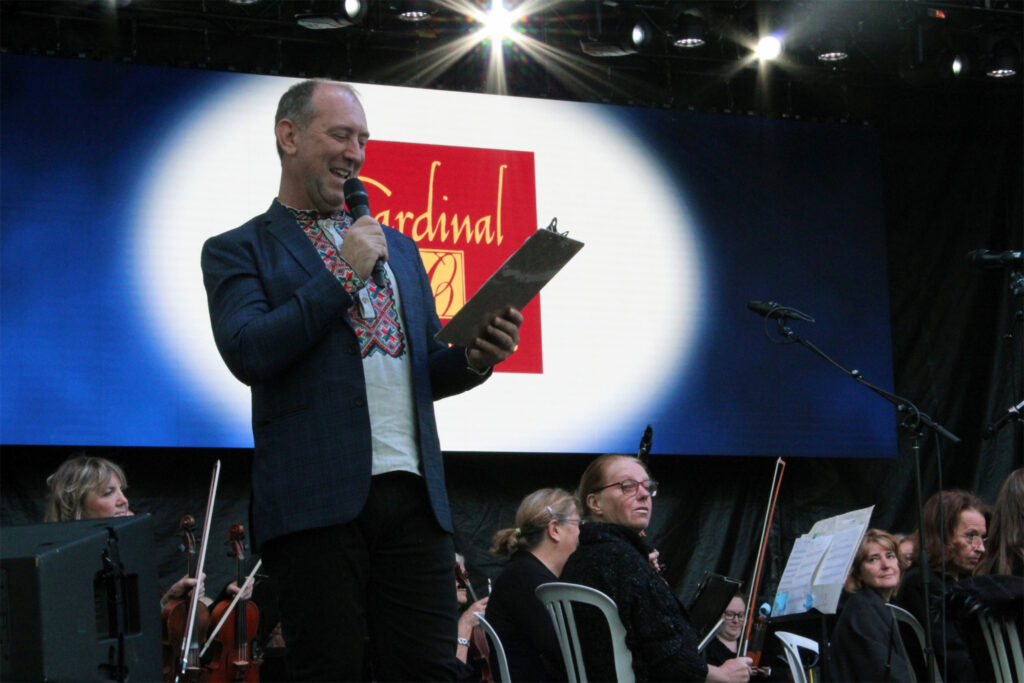 A man in a traditional Ukrainian garment stands on stage with a microphone smiling. 