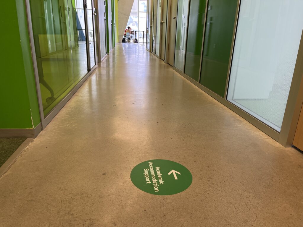 Hallway with a sign on the floor pointing to the offices of Academic Accommodation Support