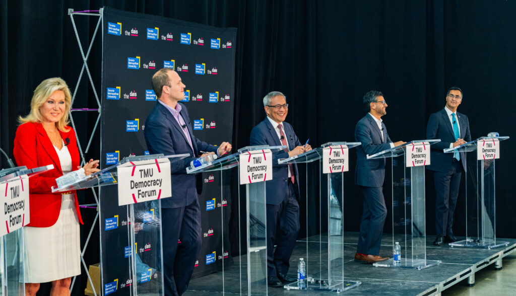 Five candidates standing at their podiums on a stage.