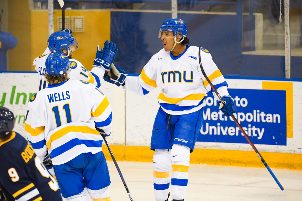 Hockey players on the ice in TMU blue and gold uniforms.