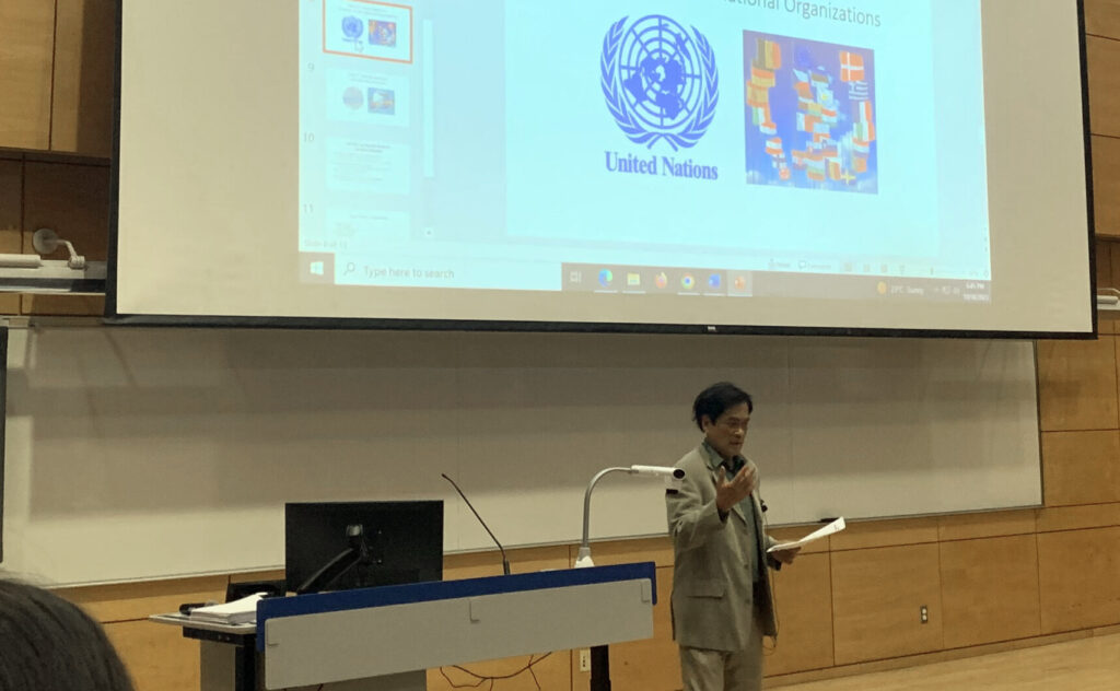 Photo of a man speaking with a mic in front of a presentation projected behind him.