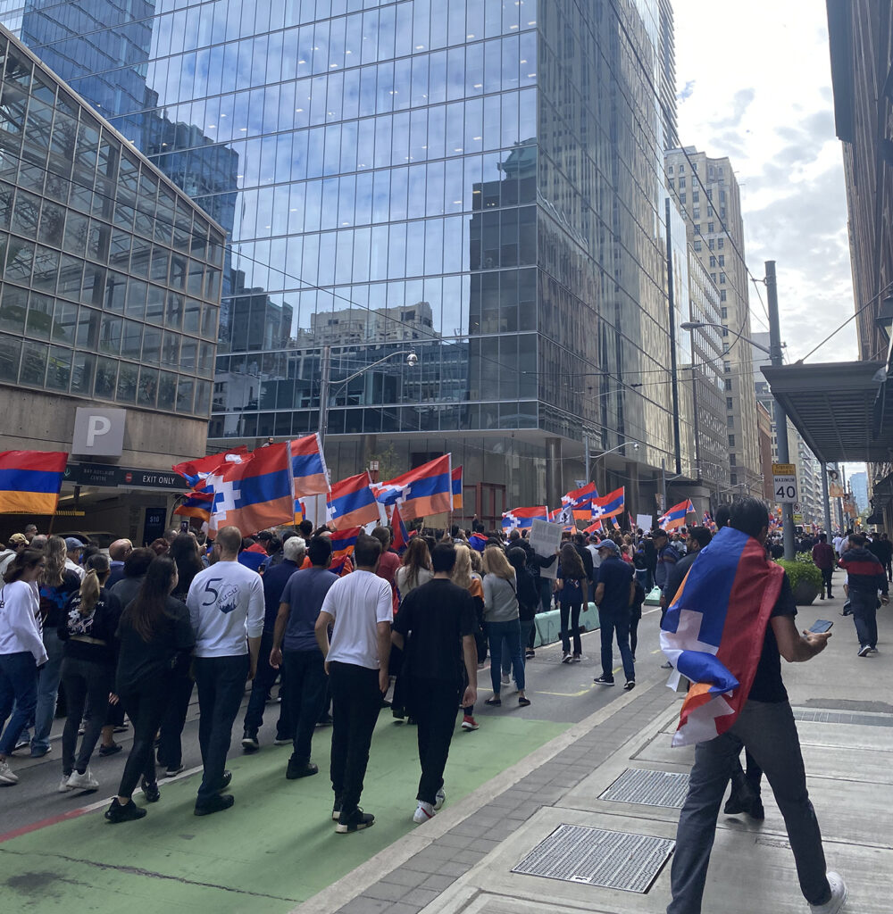 A photo of a crowd of people walking away from the camera, carrying flags.