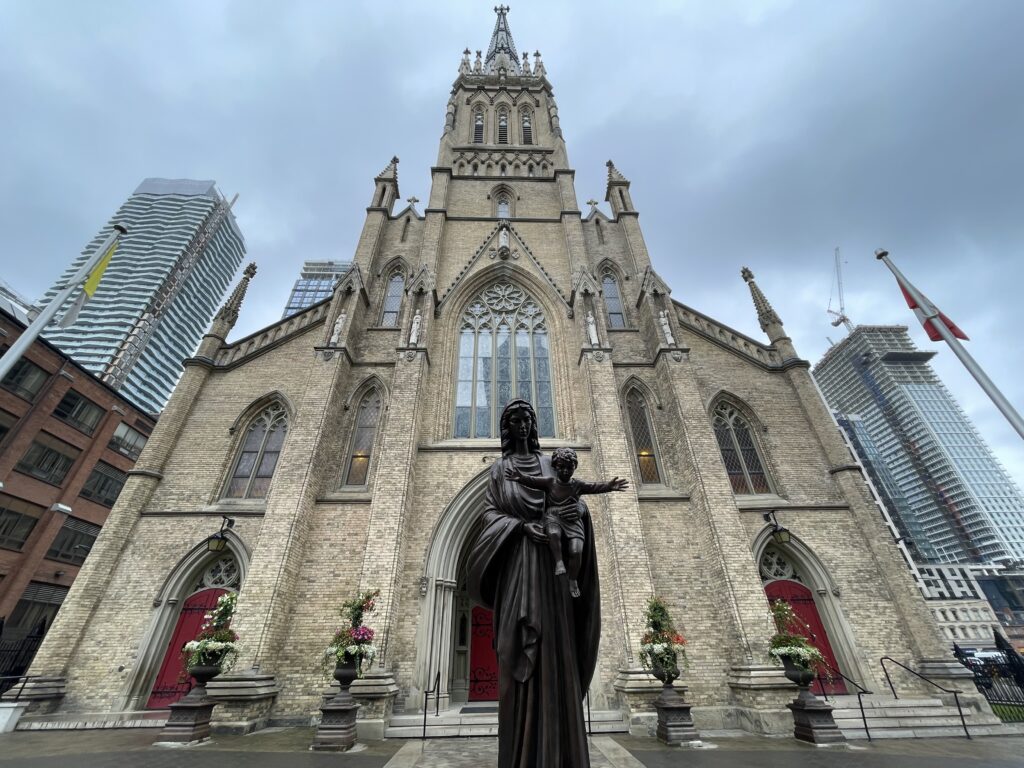 An image of the front entrance of St. Michael's Cathedral Basilica, with a statue of Mary holding baby Jesus in the foreground.