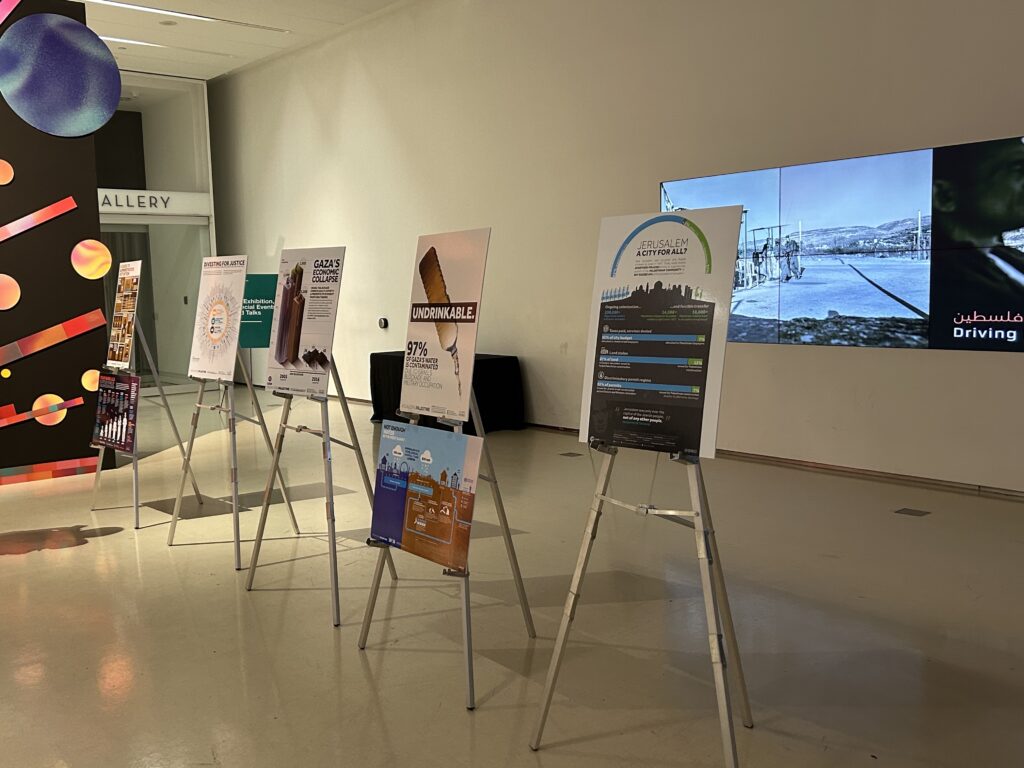 Exhibit of infographics explaining the situation in Palestine, with a film playing in the background. The posters speak of the racial inequalities and uneven distribution of resources in Palestine and Israel.