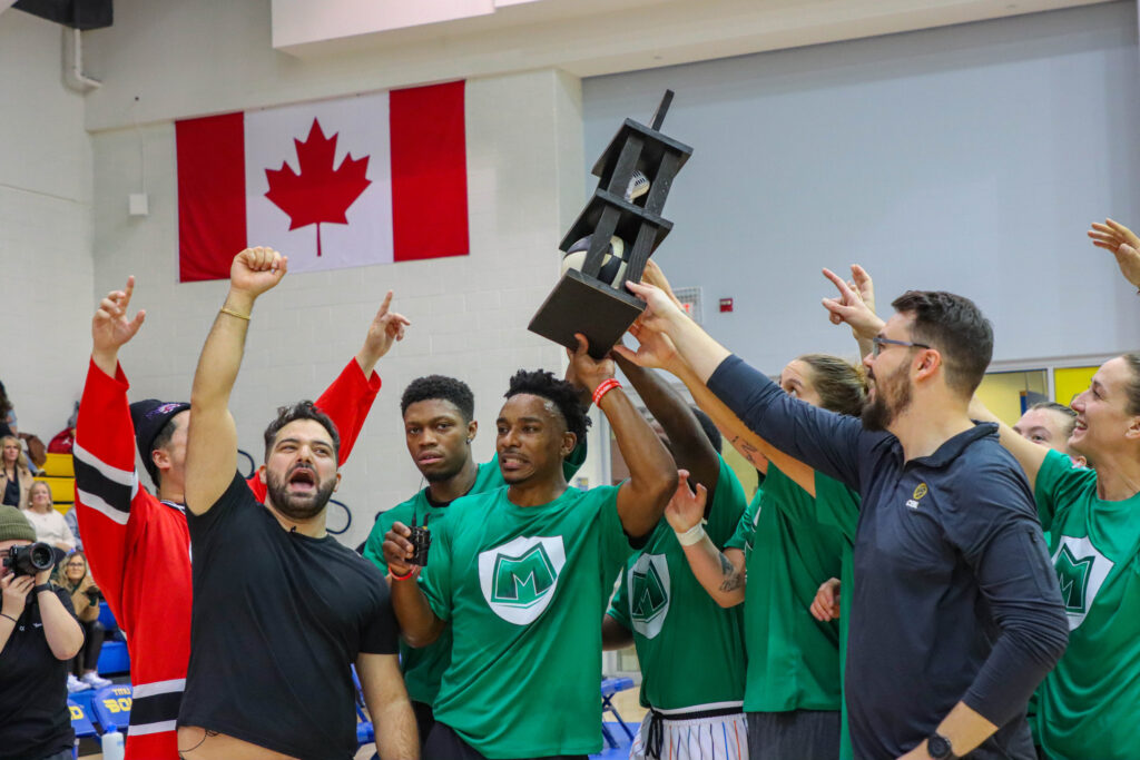 Green-shirted team holding up trophy in gym with Canadian flag in background