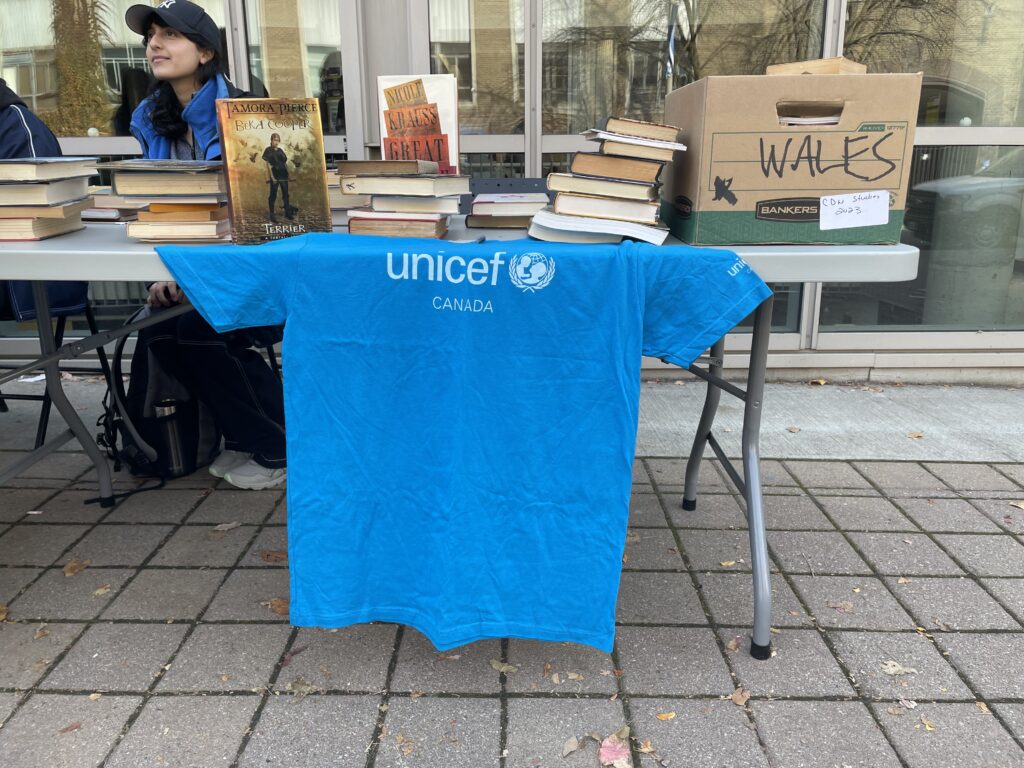 Blue UNICEF t-shirt is laid out in front of a table, held under stacks of books