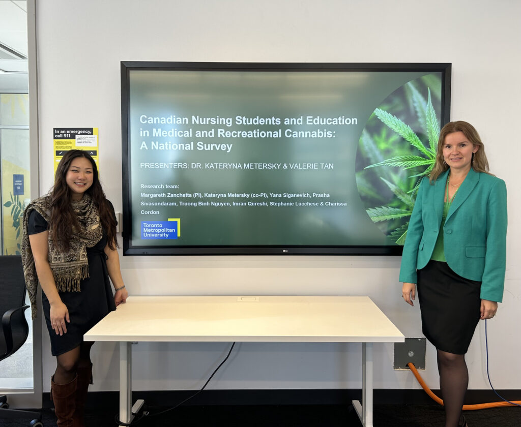 A woman dressed in a black dress with a scarf stands beside a screen with the words "Canadian Nursing Students and Education in Medical and Recreational Cannabis: A National Study." Beside the screen to the right is a woman in a green blazer and black skirt.