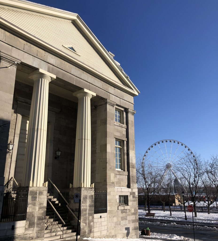 A photo of the old court house near Montreal City Hall, a grey stone building with steps and in the background you can see a ferris wheel and a stop sign.