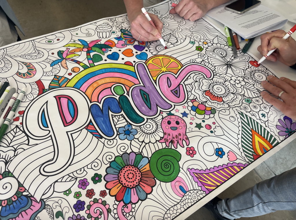 Four hands colouring in a half-filled Pride banner.