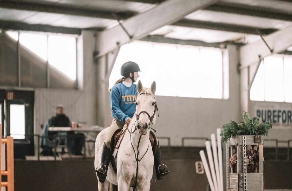 TMU female student on a white horse in an equestrian stable.