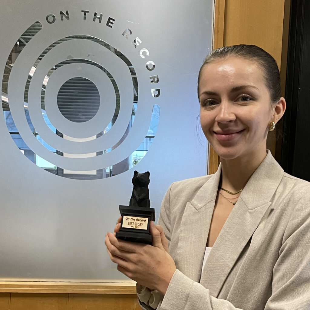 Photo of Mariya holding the TKTK award in front of the OTR newsroom door.