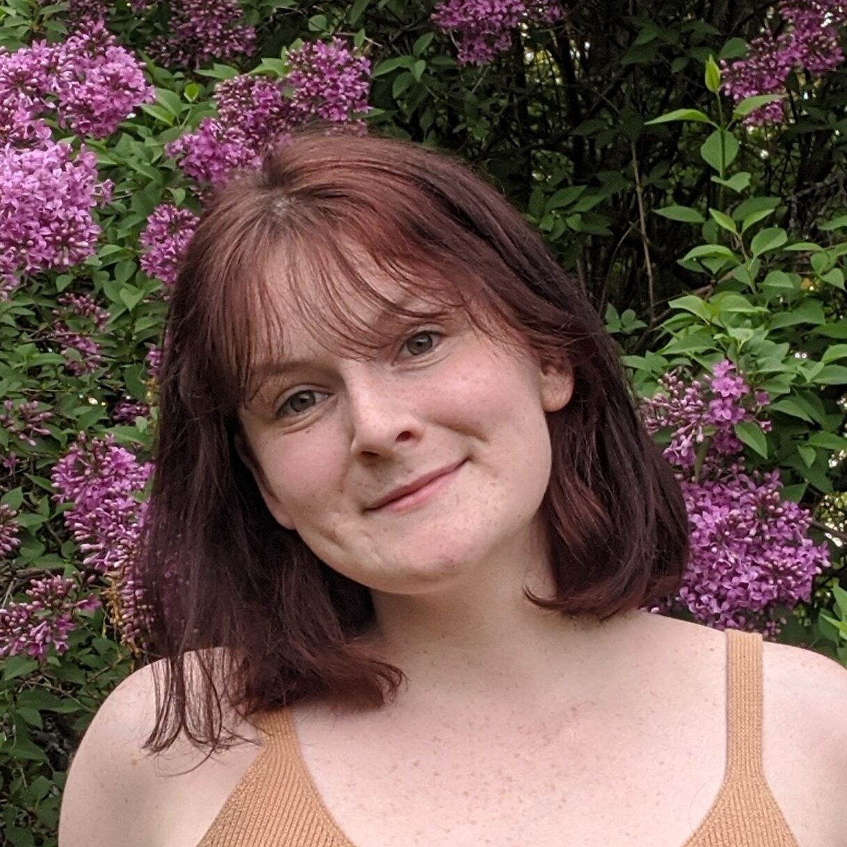 A woman wearing a yellow tank top in front of a purple lilac tree.