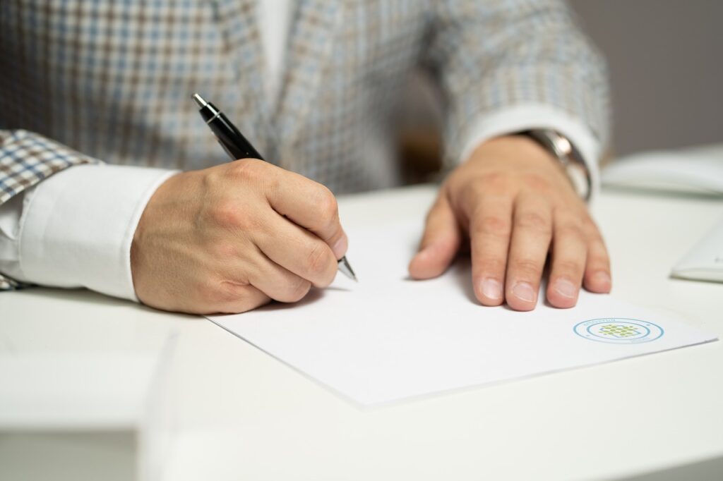 Image of someone signing a contract with a pen whilst wearing a suit.