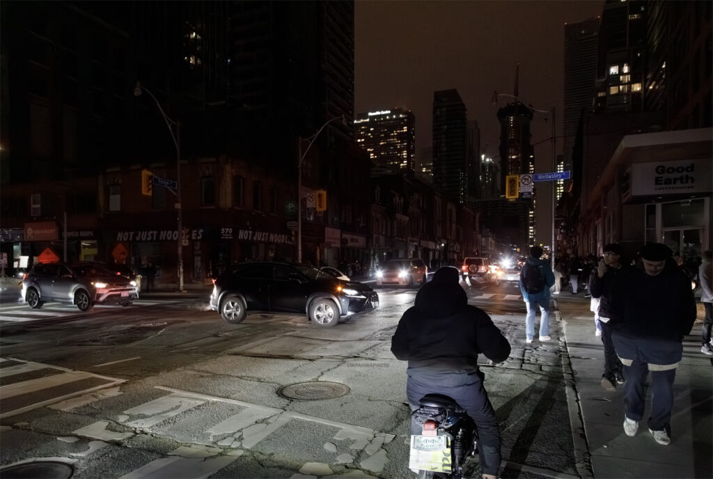 A picture of the intersection of Yonge and Wellesley with the streetlights out as cars and pedestrians navigate a blackout.