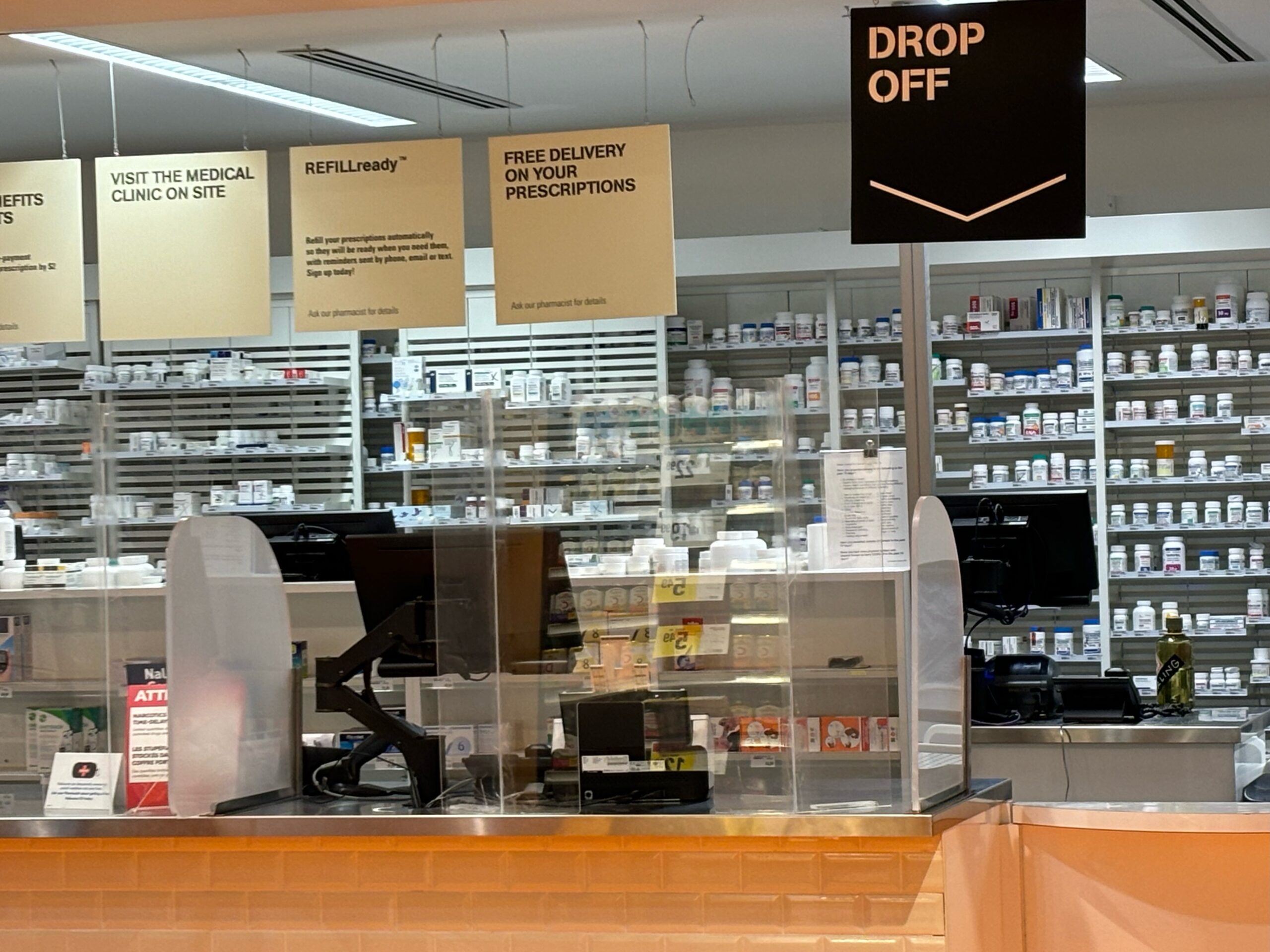 A photo showing a pharmacy with glass, and prescription bottles on shelves.
