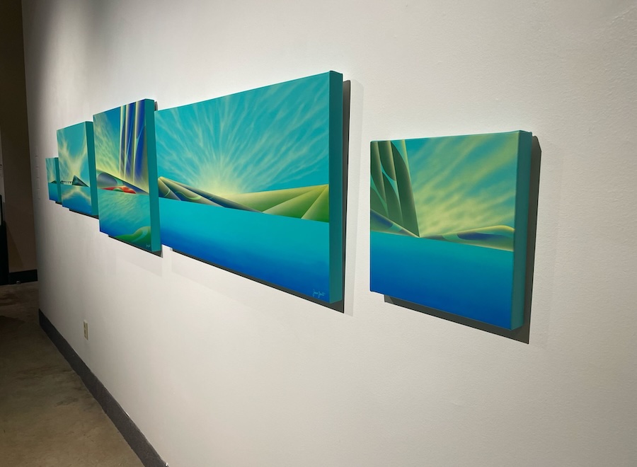 A group of paintings in teal on a white wall.