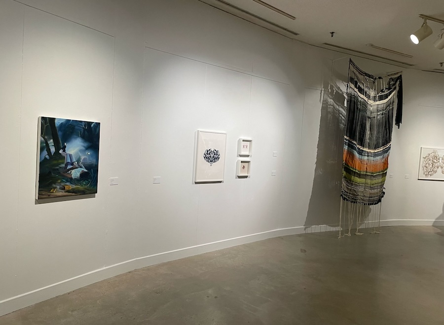 A painting and art in fabric hanging on a white wall.