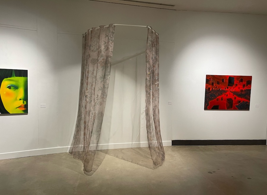 Art resembling a curtain with a painting of an Asian person's face on one side and a painting of black boxes floating in a red room.