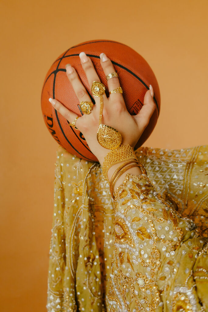 Photo of hands holding basketball. Hands have gold south asian jewlery on and is wearing gold south asian clothes.