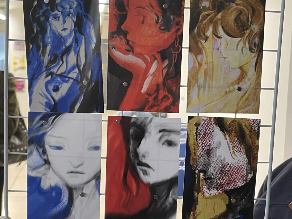 Six portraits of a woman, done in yellow, red, and blue, hang for sale on a wired rack.