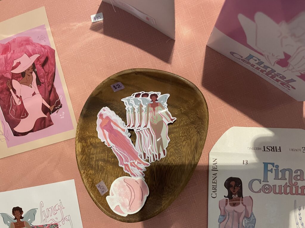 A handful of stickers for sale in a wooden bowl surrounded by small fashion portrait drawings.
